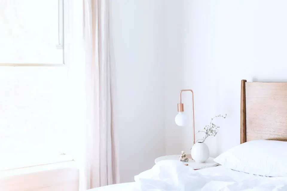 A bedroom with a wide window and neutral linen.