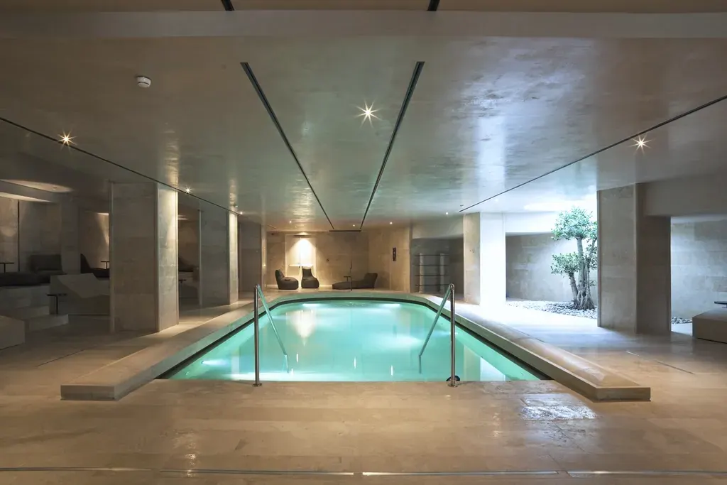 An indoor swimming pool lit from below, with timber ceiling and stone columns