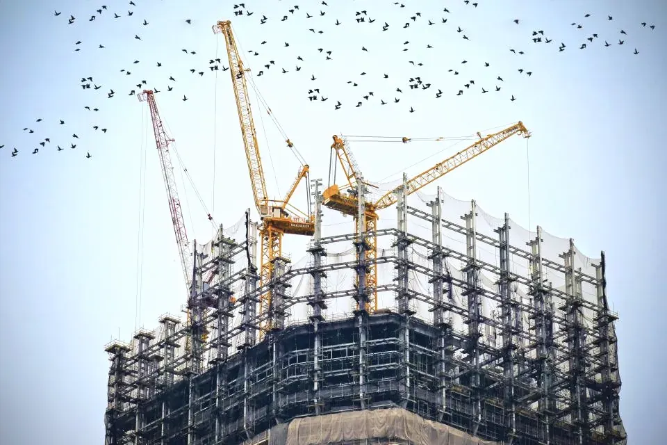 A concrete frame rising under two tower cranes
